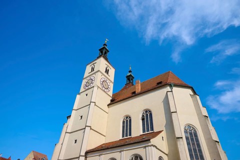 View of a church with a prominent steeple and clock against a clear blue sky, Neupfarrkirche,