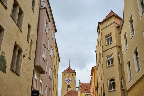 View of a tower through narrow alleys of historic buildings under a grey sky, Regensburg, Bavaria,
