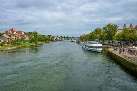 River landscape with boats and houses along the shore under a cloudy sky, Danube, Regensburg,
