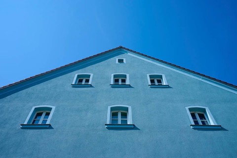Blue house with several windows and sloping roof in front of a bright blue sky, Regensburg,