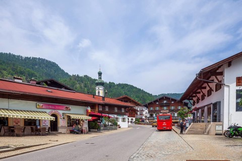 Village scene with houses, shops, bus, town hall and parish church St. Pankratius, Reit im Winkl,