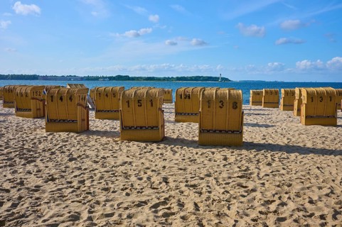 Row of numbered beach chairs under a blue sky on a sunny sandy beach, Heikendorf, Plön district,
