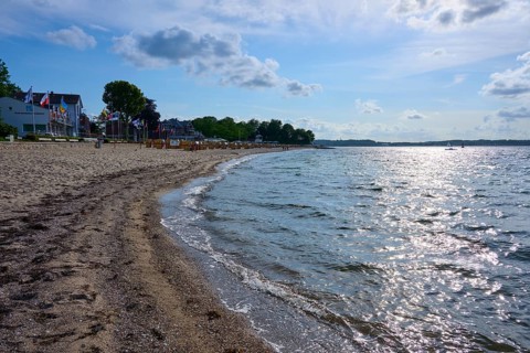 Sandy beach beach with undulating sea under a blue sky, the sun reflected on the water, Heikendorf,