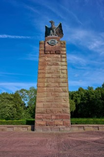 Massive memorial with eagle at the top, surrounded by trees, under a clear blue sky. Means strength