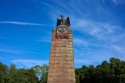 Massive stone monument with eagle, under a bright blue sky. Impression of grandeur and freedom in