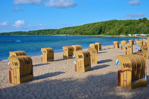 Beach chairs on a sandy beach with a wooded background and calm sea, Heikendorf, Plön district,
