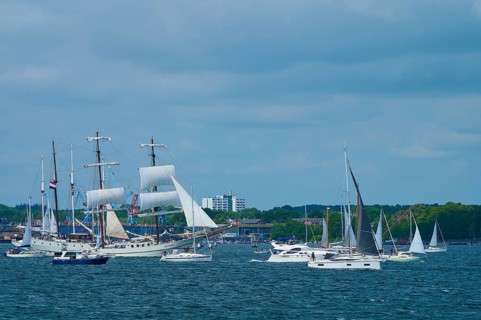 Boats and large sailors on the sea in front of a city under a blue sky, Windjammer Parade Kiel