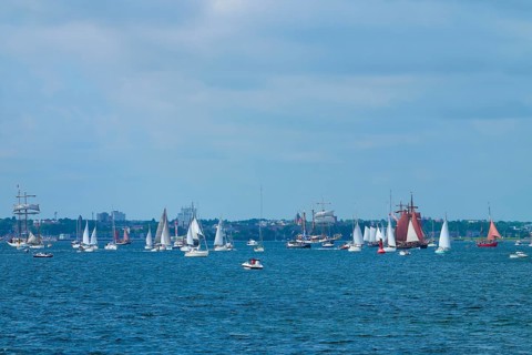 Many sailing boats in front of a city on the blue sea under a partly cloudy sky, Windjammer Parade
