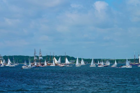 Numerous sailing boats and a large sailing ship on the open sea with a coastal view, Windjammer