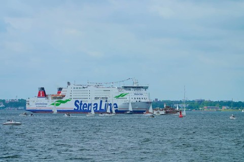 Large Stena Line ferry on the sea, surrounded by smaller sailing boats under a cloudy sky,