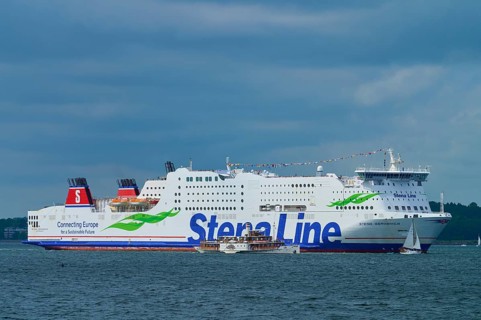 Large Stena Line ferry on the sea, accompanied by smaller sailing boats under a cloudy sky,