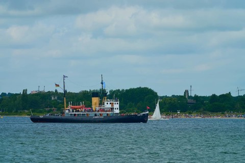 Historic icebreaker Stettin and a small sailing boat in front of a green coastal landscape and