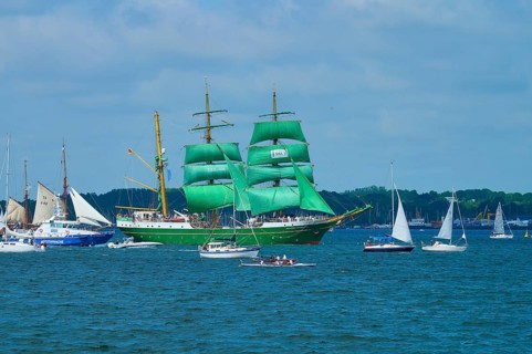 A large sailing ship with green sails Alexander von Humbold 2 and a group of smaller boats on the