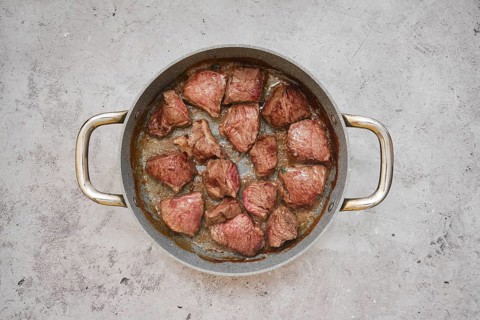 Chunks of beef are sizzling in a frying pan, showcasing a delicious golden-brown crust in the