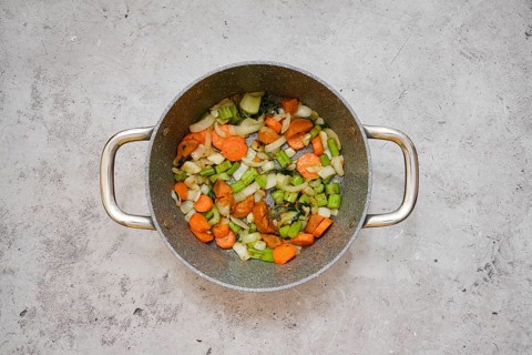 Chopped carrots, celery, and onion are frying in a pot, creating a vibrant vegetable base mixture