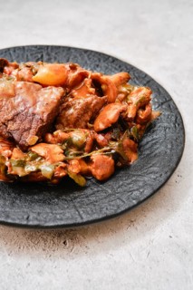 A flavorful combination of tender meat and a medley of vegetables on a black plate. The dish