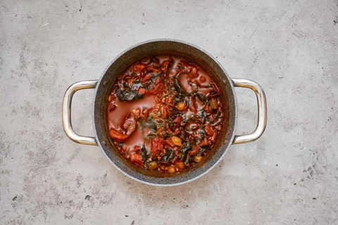 A large pot filled with a flavourful beef and vegetable stew on a gray kitchen countertop.