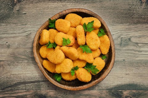 A generous serving of golden chicken nuggets is arranged in a rustic wooden bowl, garnished with