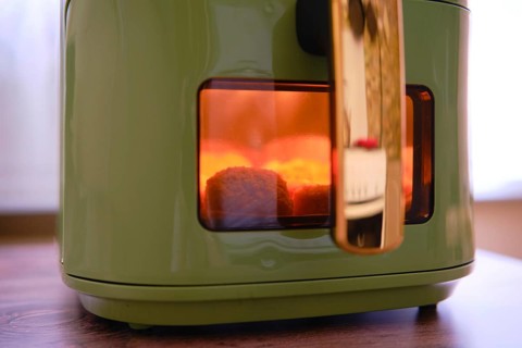 Golden-brown chicken nuggets are cooking in an air fryer, with a warm glow visible through the