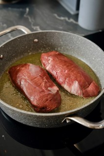 Two duck breasts are sizzling in a pan with hot fat, infusing the kitchen with rich aroma