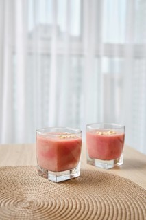 Two elegant glasses filled with a vibrant banana-strawberry smoothie sit atop a woven placemat on a