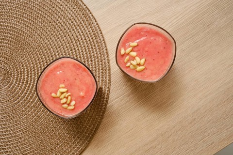 Two glasses filled with a creamy banana-strawberry smoothie sit on a natural-colored table. Topped