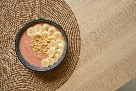 Bright and colorful banana strawberry smoothie is topped with fresh banana slices and pine nuts,