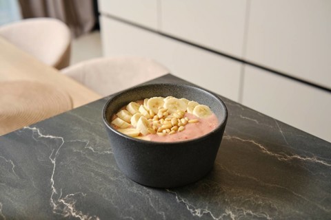 Bright and inviting banana-strawberry smoothie sits in a dark bowl, garnished with fresh banana