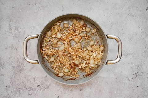 A silver pan contains a mixture of caramelized pearl onions and chopped shallot, creating a savory