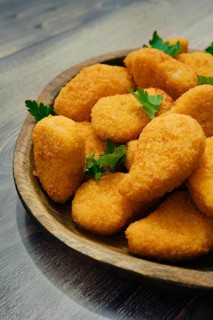 Close-up view of golden-brown chicken nuggets in breading on a rustic wooden platter. The crispy