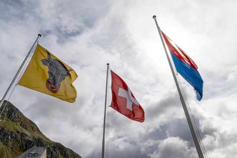 Flags of the cantons of Uri and Ticino and the Swiss flag waving in the wind, Gotthard Pass,