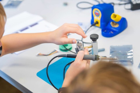 Person soldering electronic components on a workbench with a soldering iron, Youth Research Centre