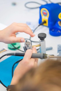 Close-up of two hands working with a soldering iron on a technical device, Youth Research Centre