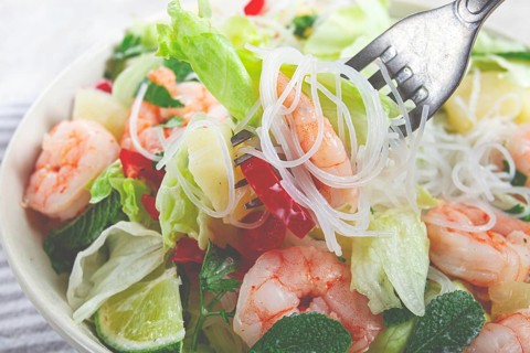Thai salad with shrimp and rice noodles, pineapple slices, coriander and mint leaves, on a white