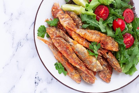 Fried crispy mullet fish, with fresh salad, on a plate with lime, no people