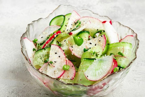 A vibrant vegetable salad is prepared with slices of radishes and cucumbers, garnished with herbs