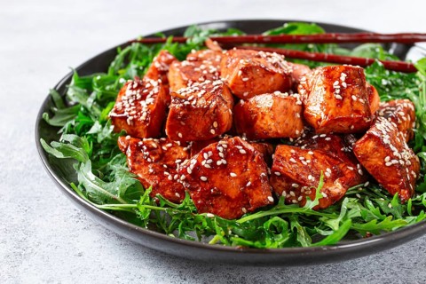 Fried salmon slices, teriyaki with sesame seeds, with arugula salad, top view