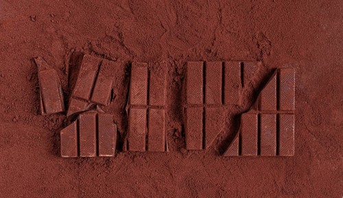 Chocolate bars broken and scattered on cocoa powder background with rich texture and color