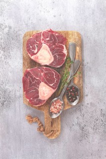 Freshly sliced beef legs, two ossobuco steaks, on a wooden board, with spices and herbs, ready to