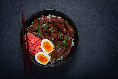 Udon Japanese beef with rice, pickled ginger, boiled egg slice, garnished with green onions, in a