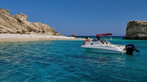 Motorboat drifting in the clear blue sea in front of a rocky coastline, White Cliffs, White Beach,