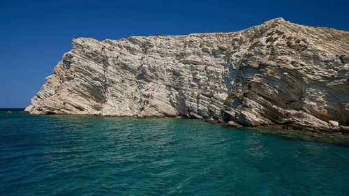 An imposing cliff rises above the blue sea under a bright sky, White Cliffs, White Beach, Makri