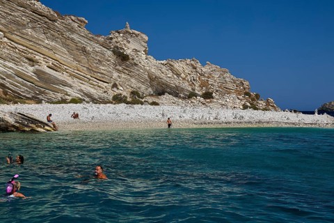 People swimming in calm turquoise waters off a rocky coast, White Cliffs, White Beach, Makri
