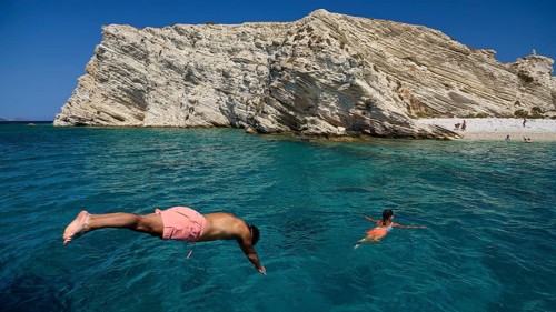 People swimming in clear blue water in front of impressive rocky cliffs, White Cliffs, White Beach,