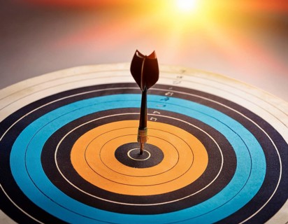 A precise dart accurately hitting the bullseye of a circular target against a vivid blue backdrop,
