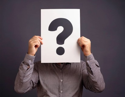 A person concealing their face while holding a question mark sign, symbolizing anonymity, mystery,