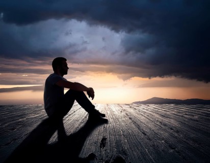Silhouette of a person sitting alone within a brick archway, observing a peaceful and scenic cloudy