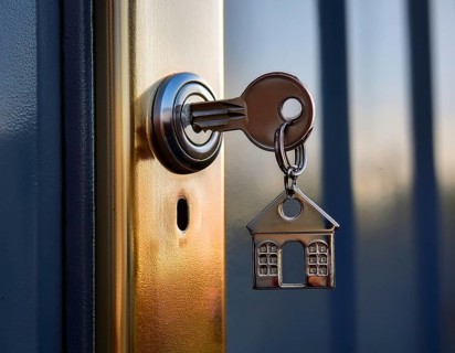 A key with a house-shaped keychain inserted into a keyhole, symbolizing home security and property