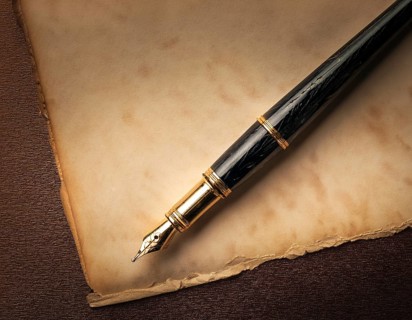 Close-up of a classic fountain pen lying atop old aged paper on a wooden surface, symbolizing