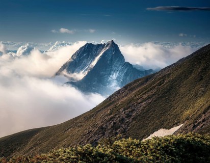 A stunning view of a snowy mountain peak rising above the clouds, with a blue sky background.